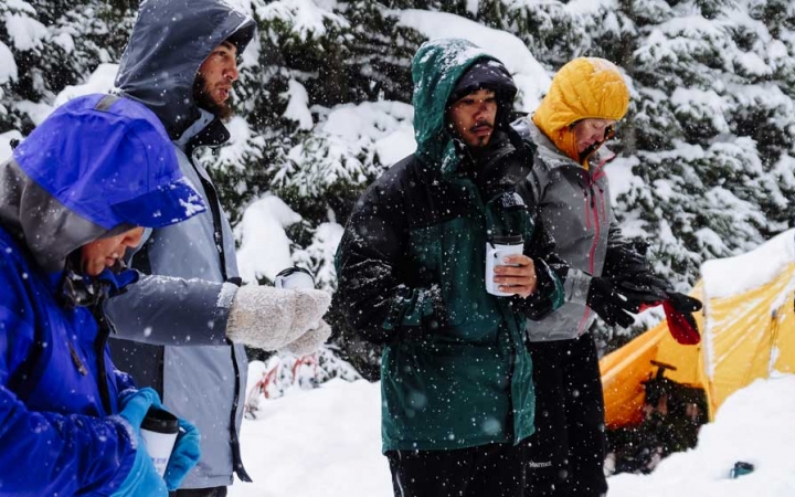 a group of veterans wearing snow gear drink hot drinks at their campsite